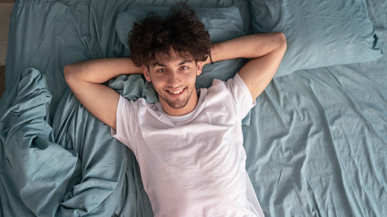 man smiling up at camera while lying on blue-gray microfiber sheets