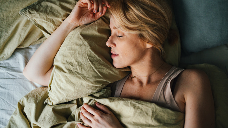 a blonde woman is falling asleep in a light olive green linen bed sheet set