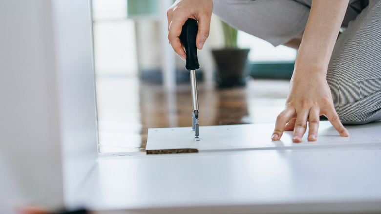 person screwing a screw into a white piece of wood with a screwdriver