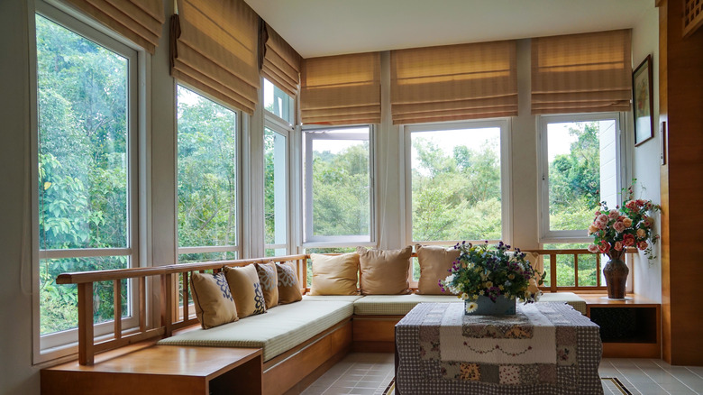 sun porch with a built in bench, wall-to-wall-windows, and striped Roman shades