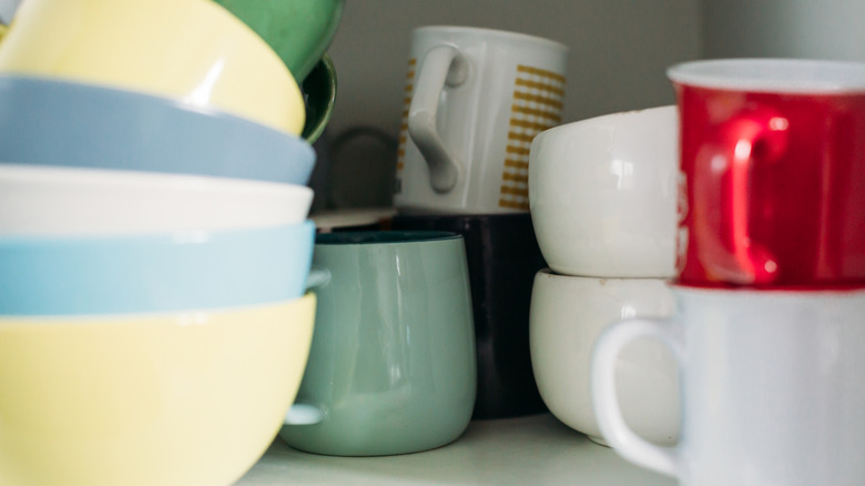 assortment of mugs stacked up haphazardly in a white cabinet