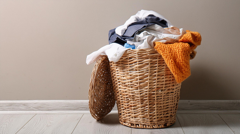 wicker laundry basket full of dirty clothing items sitting on a floor against the wall