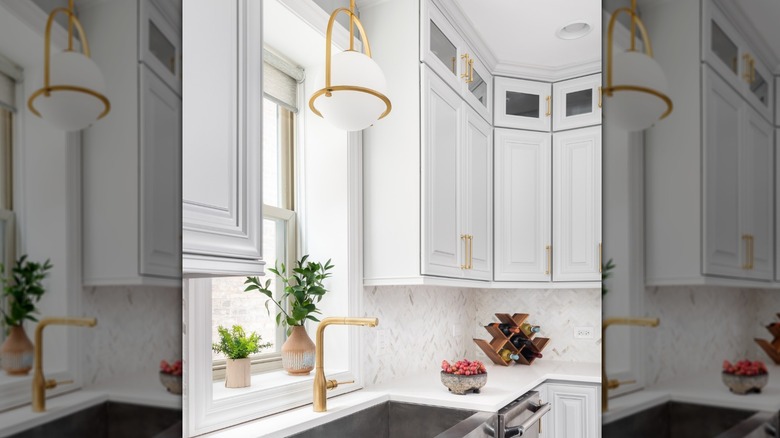 modern kitchen with white cabinets, brass hardware, and a stainless steel apron front sink with a brass globe light fixture hanging above it in front of a window