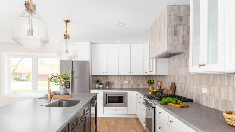 modern kitchen with white cabinets, beige varied vertical tile, taupe countertops, and two oversized brass and glass light fixtures over the island