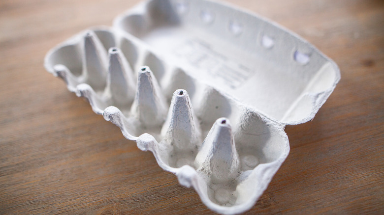 An empty cardboard egg carton set against a wooden table