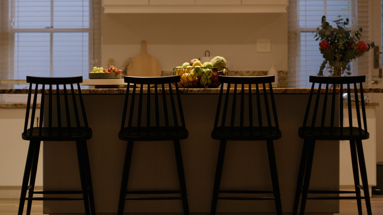 A kitchen countertop with four identical chairs is dimly lit by a pair of conical light fixtures.