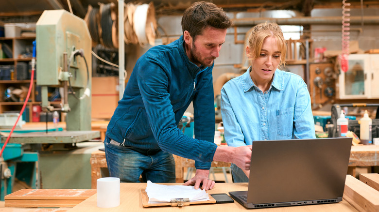 woman and man carpenters looking up information on a laptop in a wood workshop