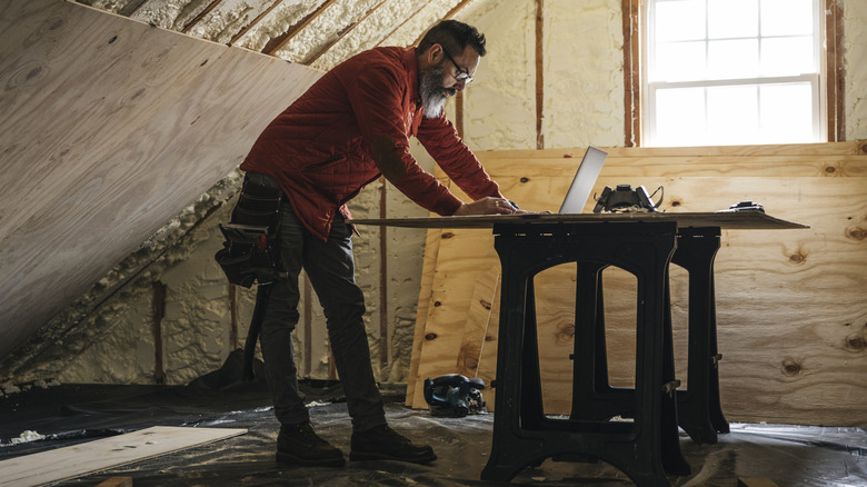 person doing home construction looking up information on laptop while surrounded by wood and insulation