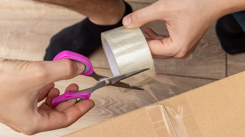 person cutting packing tape with scissors