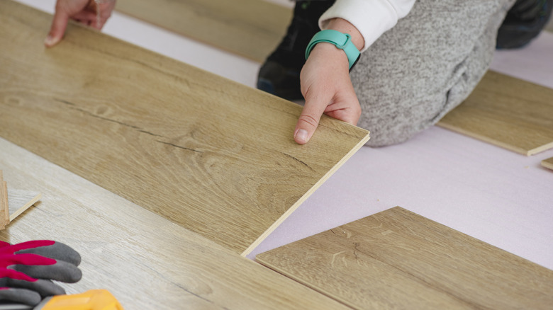 A woman is installing laminate flooring. Close up on her hands as she places a board on the subfloor.