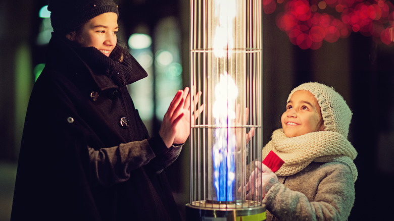 Two kids warming their hands on an outdoor propane heater