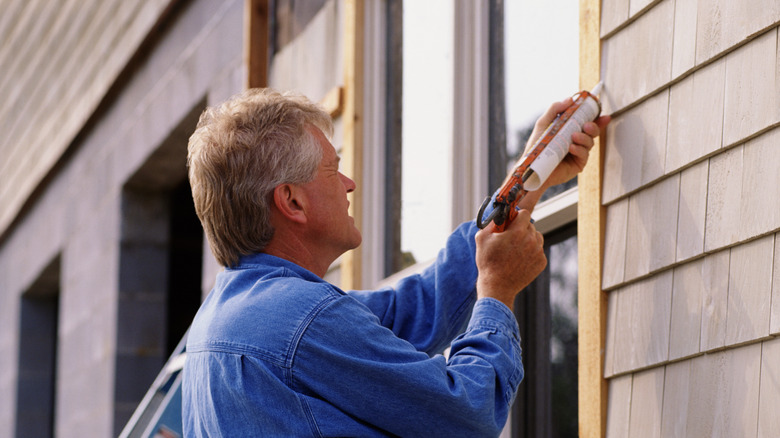 Man adding caulk to window exterior