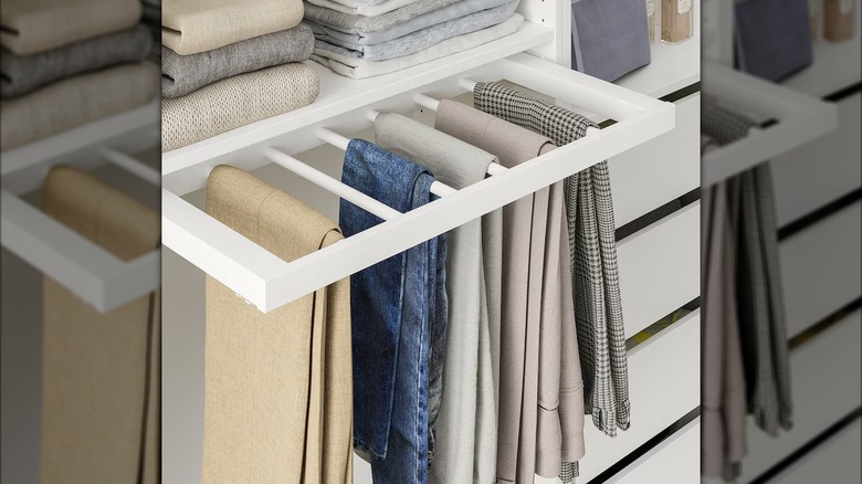 white IKEA pull-out pants holder installed under a shelf in the closet and containing five pairs of pants draped over the dowels