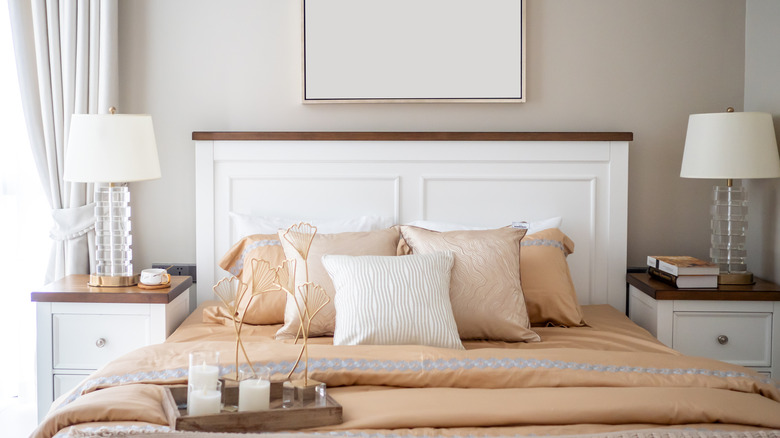 Bedroom with nightstands, lamps, bed with clay-colored sheets, white headboard, beige paint