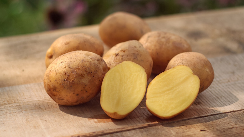 bunch of raw potatoes sitting on a wood table with one cut in half