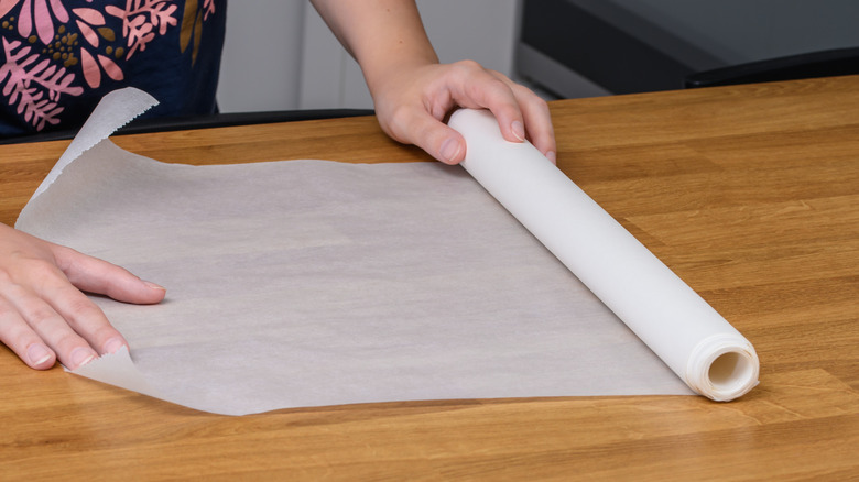 wax paper being rolled out by two hands onto a wooden counter