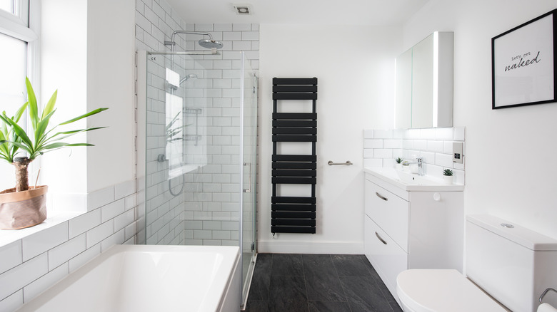 bathroom with white wall, white subway tiles, white vanity, white tub, white toilet, and chrome fixtures