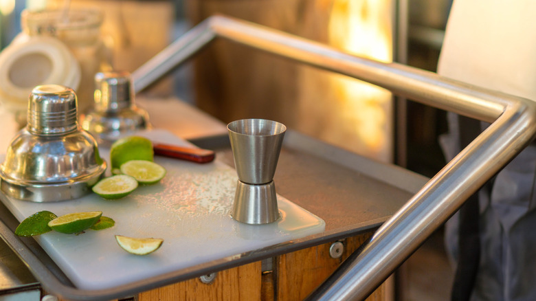 closeup of bar cart with knife, cut limes, shot measurer