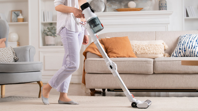 woman using a cordless upright vacuum on her off-white living room area rug