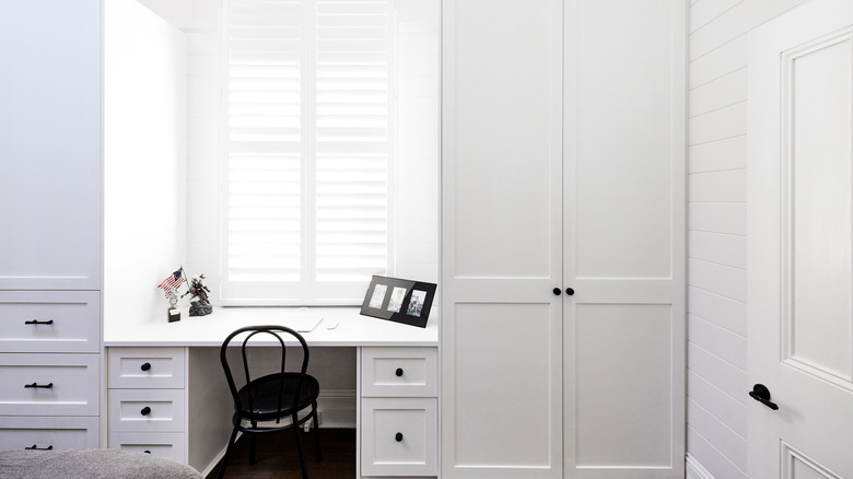 bedroom with two wall-to-wall full-height cabinets on either side of the window with white shaker style doors and a built-in desk between them