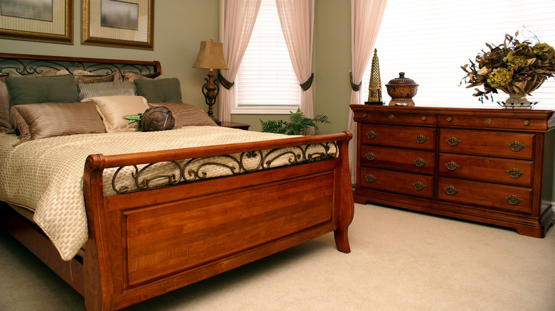 A dated-looking bedroom featuring swag curtains and a heavy wood dresser and bed frame. The room has light sage walls and beige carpet.