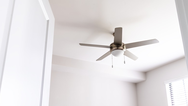 Camera is focused on the ceiling of an all-white bedroom. There is a gray ceiling fan in the middle.