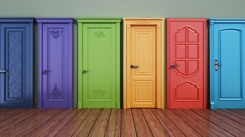 A row of colorful doors are lined up against an interior wall. Doors are painted bright colors with various carved details and moldings.