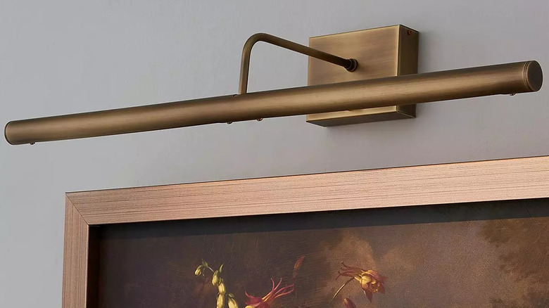 antique brass batter-operated art light hung over a moody painting of florals on a black background with a gold frame