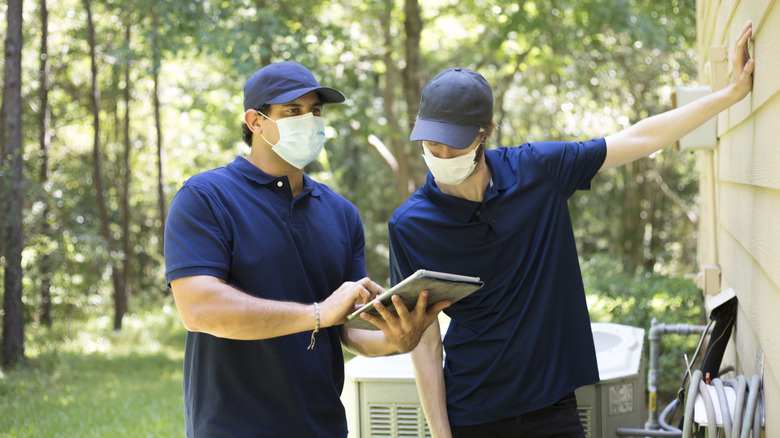 two exterminators wearing blue polos looking at outisde of a house