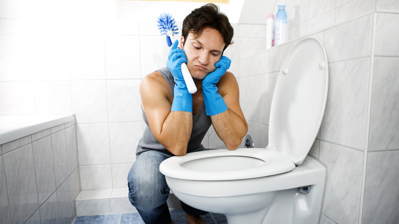 frustrated man looking at toilet while holding brush