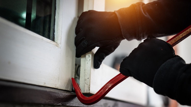 Burglar using crowbar to open window.