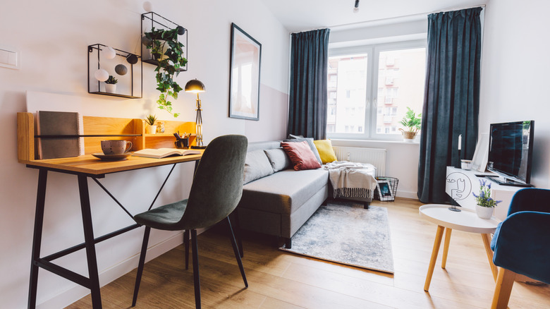 A small living space/home office with a window, couch, TV, and desk.