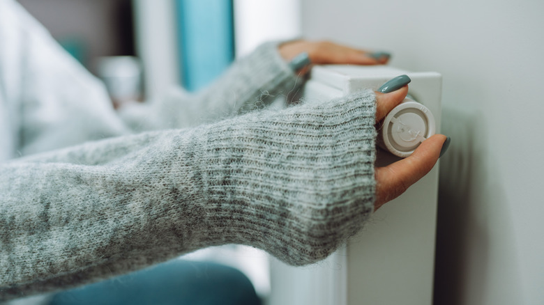 Someone with long, teal nails adjusts the thermostat dial on an indoor heater.