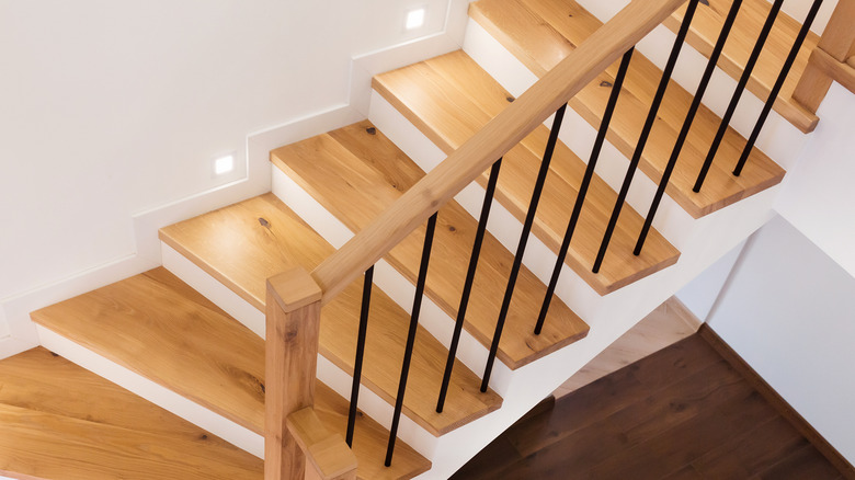 A spiraling, wooden staircase features varnished wooden handrails with plain black-bar balusters.