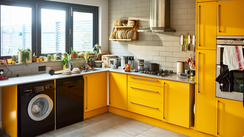 A sunny kitchen with bright yellow cabinets and black appliances including a dishwasher and washing machine.