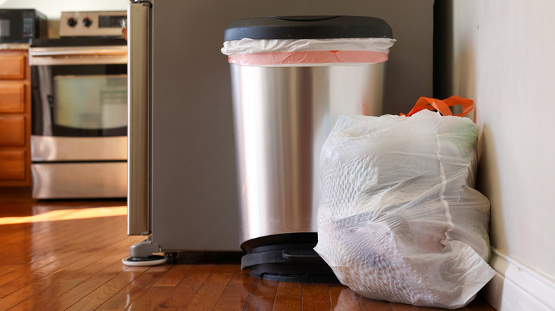 full garbage bag next to trash can